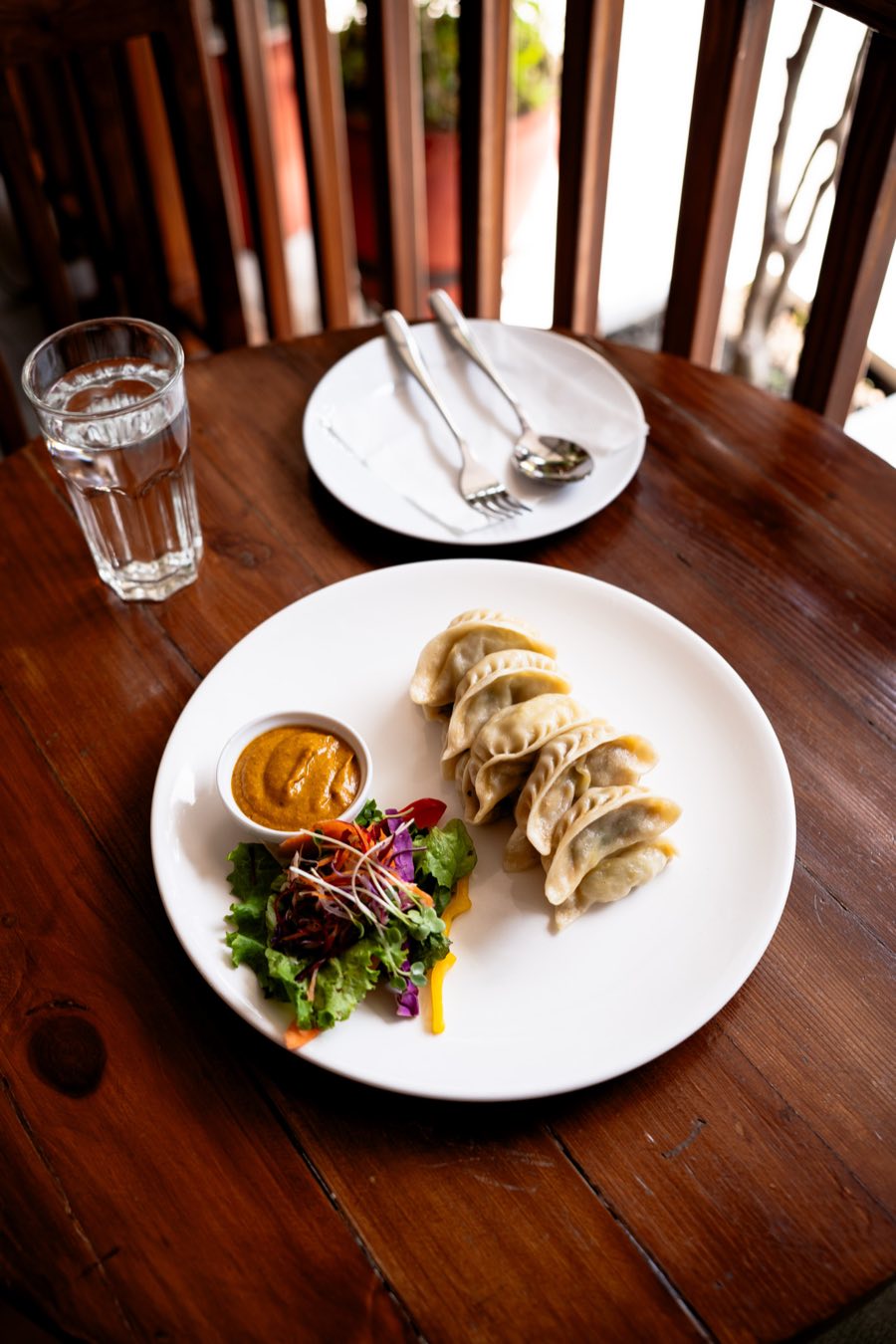 A plate of fresh Nepali momo with golden achar dipping sauce on a café balcony table in Kathmandu